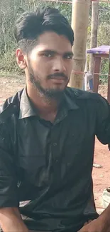 Young man in black shirt sitting outdoors.