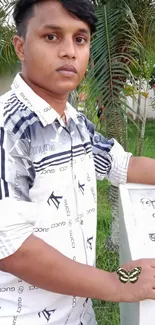 Young man outdoors in patterned shirt with green and white backdrop.