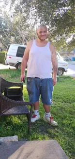 A man in casual attire outdoors with greenery and natural light in a suburban setting.