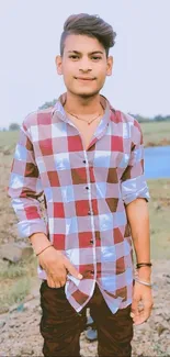 Young man in a red plaid shirt standing outdoors with a natural background.