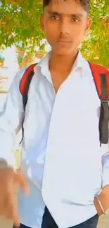 Young man with red backpack outdoors, white shirt, green background.