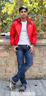 Man in a red jacket outdoors, leaning on a wall.