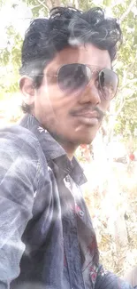 Portrait of a young man outdoors wearing sunglasses, surrounded by trees.