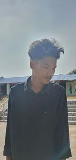 Young man posing casually in a sunny outdoor setting with a calm expression.