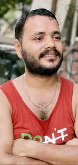 Man in red tank top smiling outdoors with blurred background.