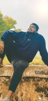 Casual man in blue hoodie sitting outdoors.