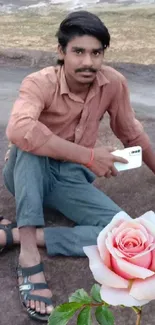 Casual man sitting outdoors with smartphone and rose.