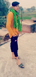 Person standing on a rural rooftop in casual attire with a green scarf.