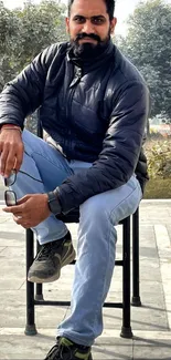 Man sitting casually outdoors with trees and concrete in background.