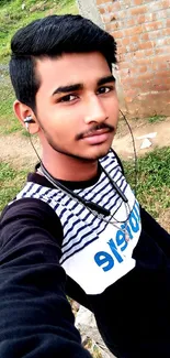 Young man takes a selfie outdoors in a casual striped shirt with a natural background.