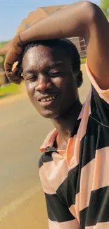 Young man smiling outside in sunlight, casual fashion.