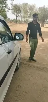 Person in casual attire with car in desert setting.