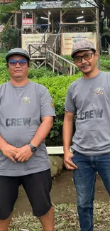 Two people in crew shirts outdoors with greenery.