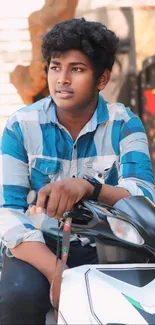 Young man in blue plaid shirt sitting on a scooter outdoors.