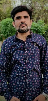 Man in a stylish patterned shirt outdoors with green background.