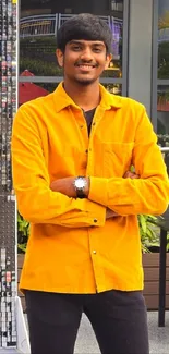 Young man in vibrant yellow shirt and black pants standing outdoors.