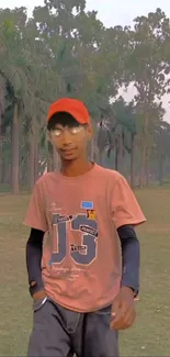 Young man in park with tall trees, wearing red hat.