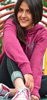 Young person in pink hoodie smiling seated in an artistic arch setting.