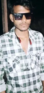 Young man in plaid shirt with sunglasses at night.