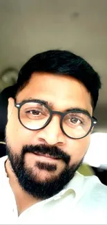 Casual portrait of a bearded man sitting inside a car, wearing glasses.