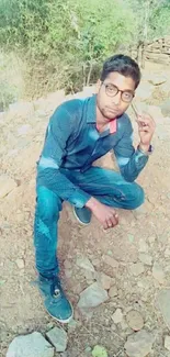 Young man in casual attire sitting on a rocky terrain with a natural background.