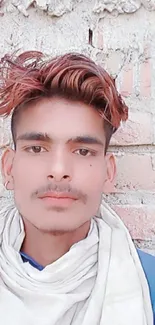 Young man in casual attire against a brick wall backdrop.