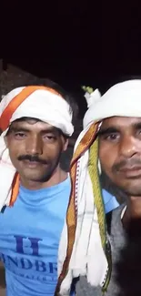 Two men with turbans in a casual portrait at night.