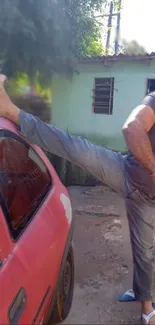 Person striking a casual pose with one leg on a red car outside.