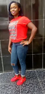 Woman in red shirt and jeans against tiled wall.