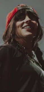 Person wearing a red cap with a playful smile on a dark background wallpaper.