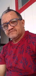 Man in red shirt with leaf pattern sitting casually.