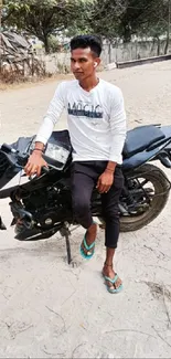 Casual rider posing on black motorcycle in sandy outdoor setting.