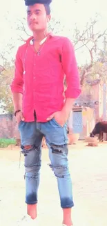 Young man in red shirt and ripped jeans in village setting.