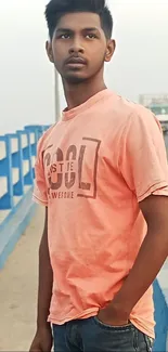 Young man in pink t-shirt standing on a bridge.