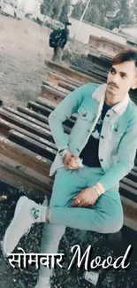 Young man in teal denim streetwear seated outdoors.