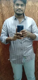 Man in striped shirt taking a mirror selfie with a brown curtain background.