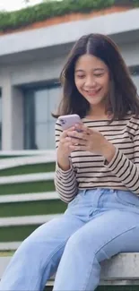 Woman in striped shirt using phone outdoors, sitting on a bench.