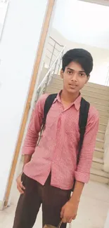 Young student posing casually indoors, holding a bag with a light background.