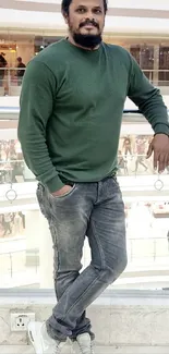 Man in a green sweater poses casually at shopping mall railing.