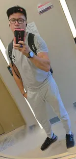 Man taking a mirror selfie in casual attire with neutral tones.