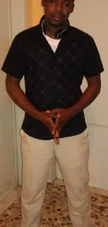 Man in black shirt and beige pants posing confidently indoors.