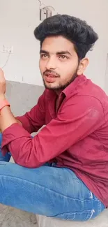 A young man in a maroon shirt and jeans on a mobile wallpaper.