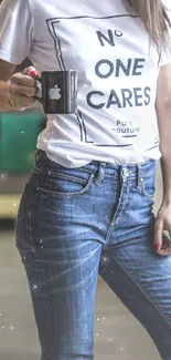 Person wearing casual jeans and a printed t-shirt holding a black mug.