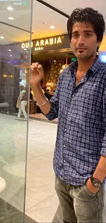 Young man in blue checkered shirt standing in a modern mall.