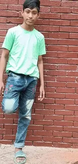 Teen boy leaning against a red brick wall in casual attire.