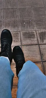 Casual view of black boots on textured brown tiles with blue jeans.