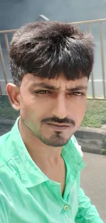 A man in a green shirt posing outdoors with a calm urban background.