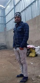 Man in plaid shirt standing in rustic warehouse.