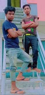 Two young men pose confidently on metal stairs in an urban setting.