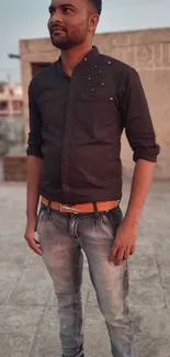 Stylish man in casual attire on a rooftop with a city backdrop.